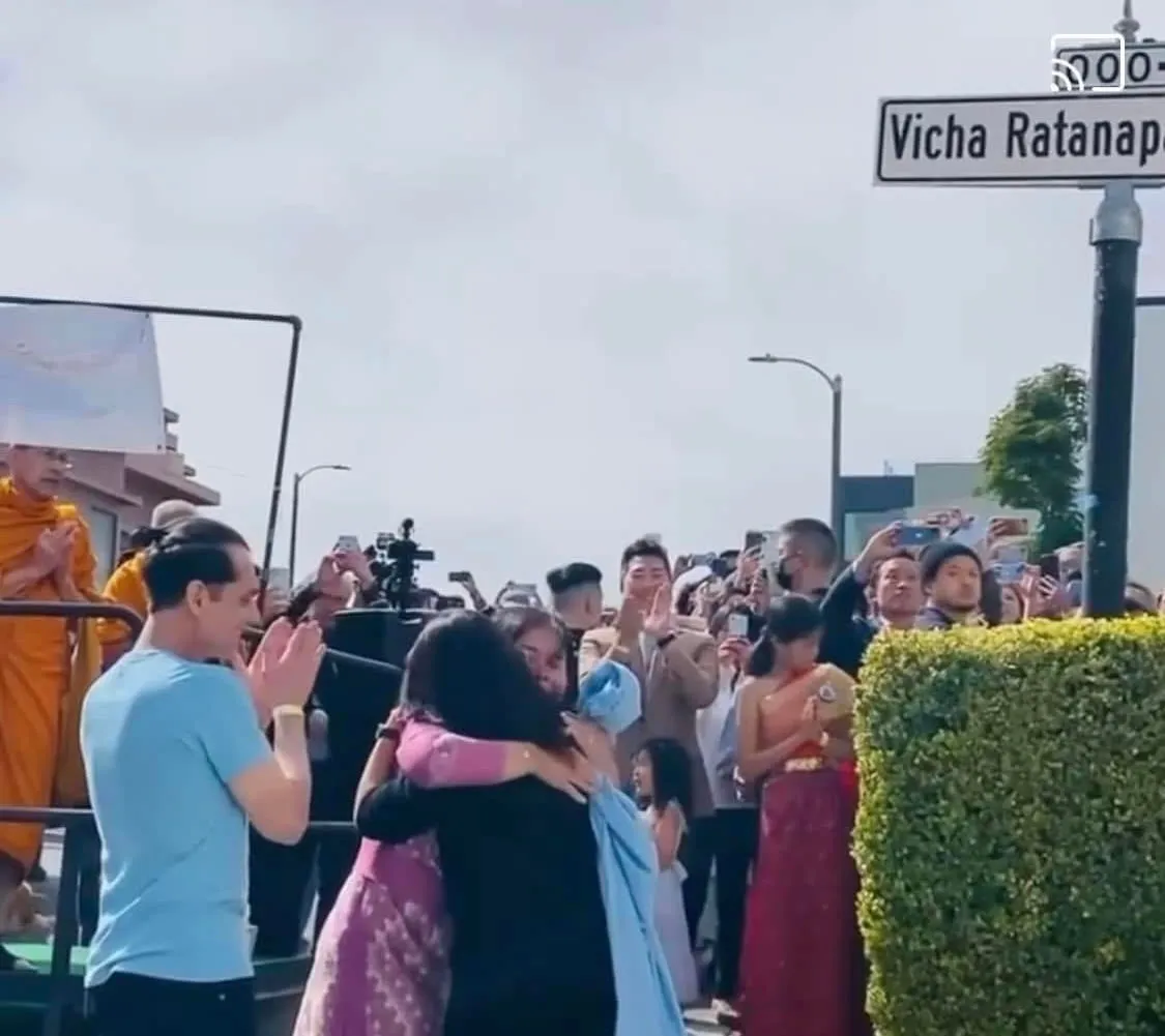 Neighbors embracing beneath the new Vicha Ratanapakdee Way street sign